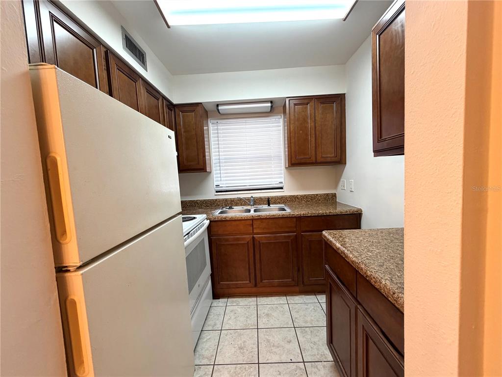 A kitchen features dark wood cabinets, granite-look countertops, a white refrigerator, and tile flooring — 710 AVENUE C SW UNIT 4A, WINTER HAVEN, FL