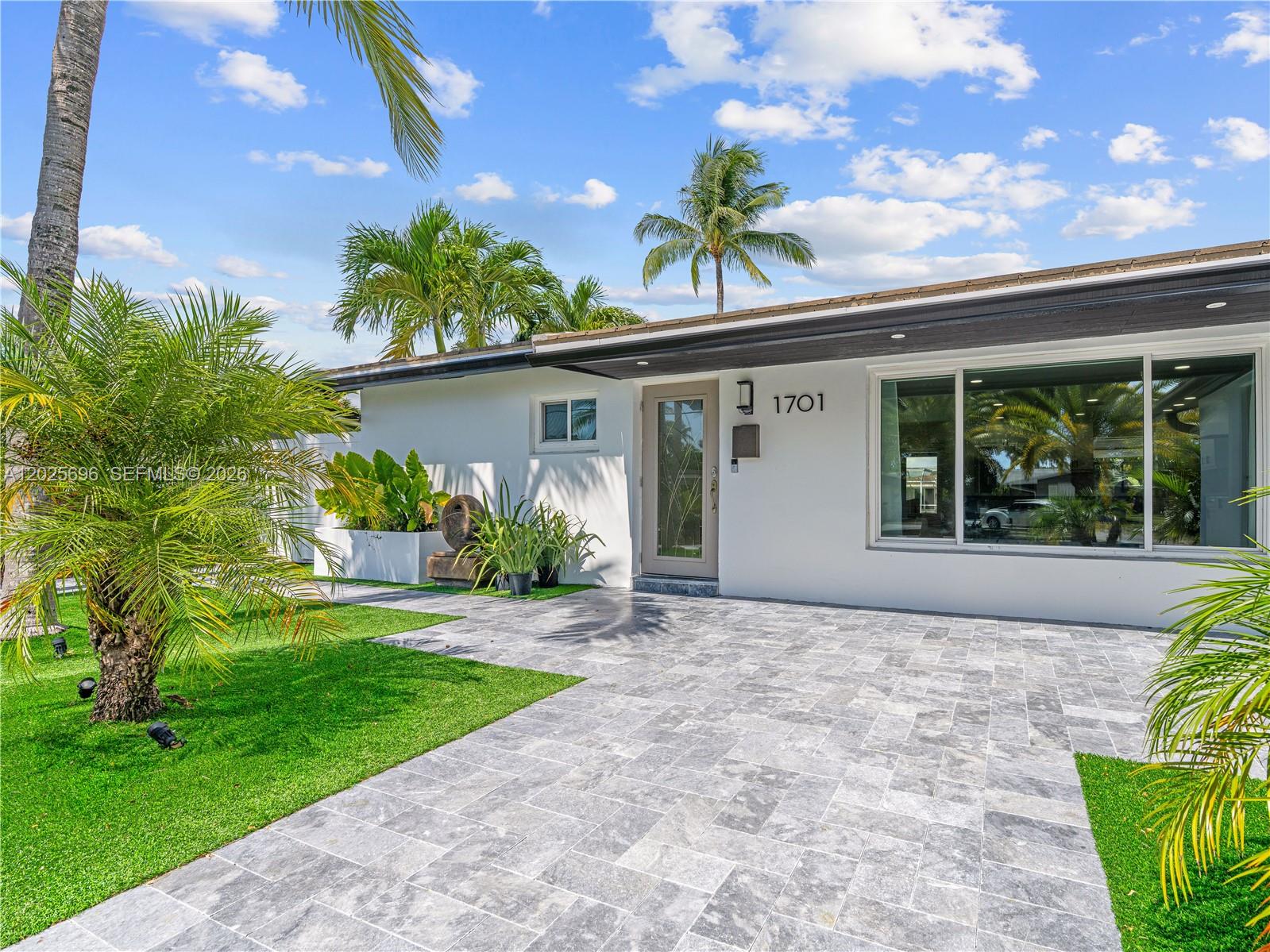 A white house exterior features a gray tiled driveway, a glass-paneled front door, and palm trees — 1701 SW 3rd Ave, Pompano Beach FL 33060, POMPANO BEACH, FL