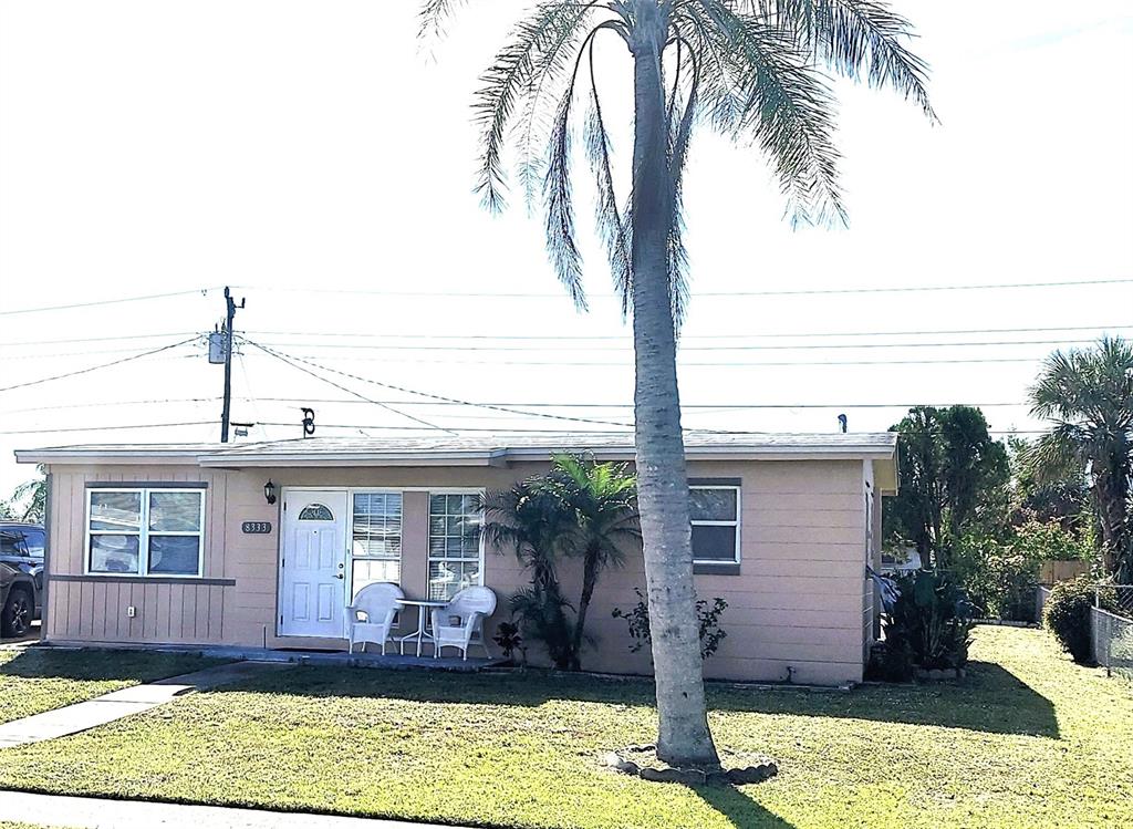 A single-story house with tan siding features a front door, white chairs, and a palm tree — 8333 HERBISON AVENUE, NORTH PORT, FL