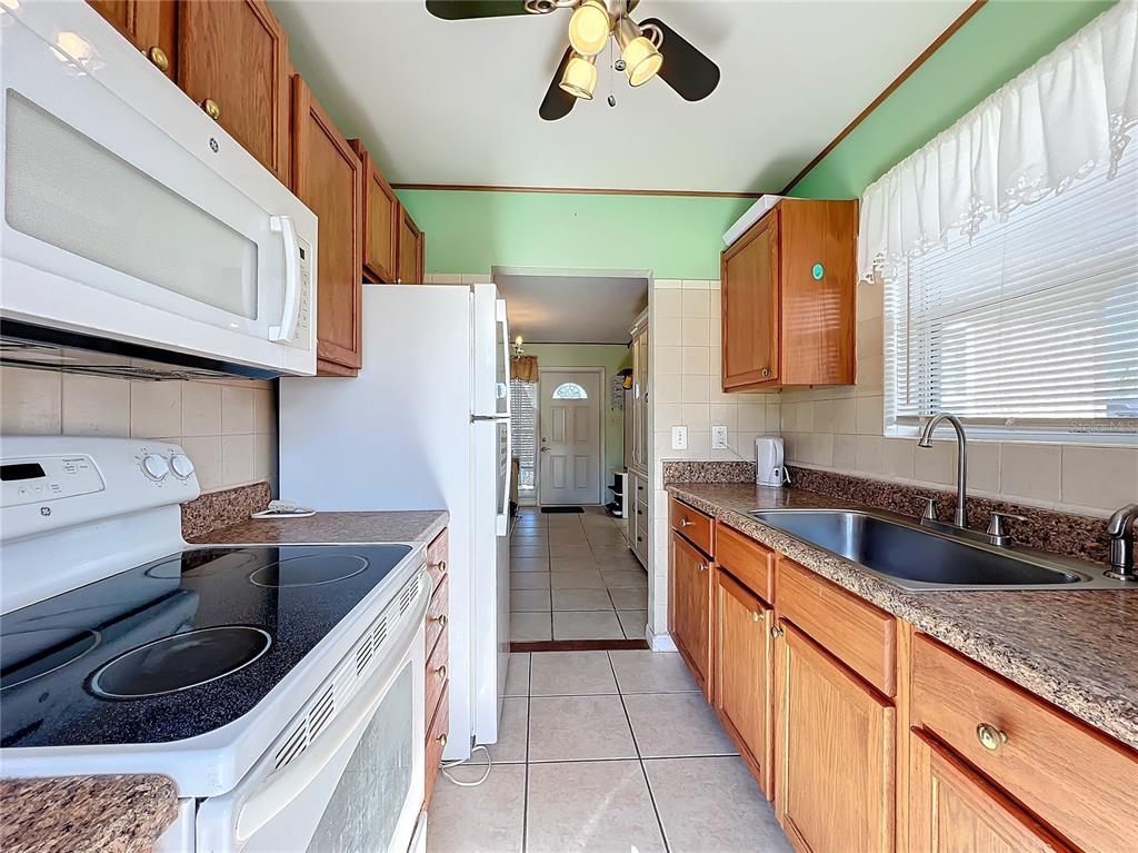 A kitchen with wood cabinets, laminate countertops, white appliances, and light green walls — 8333 HERBISON AVENUE, NORTH PORT, FL