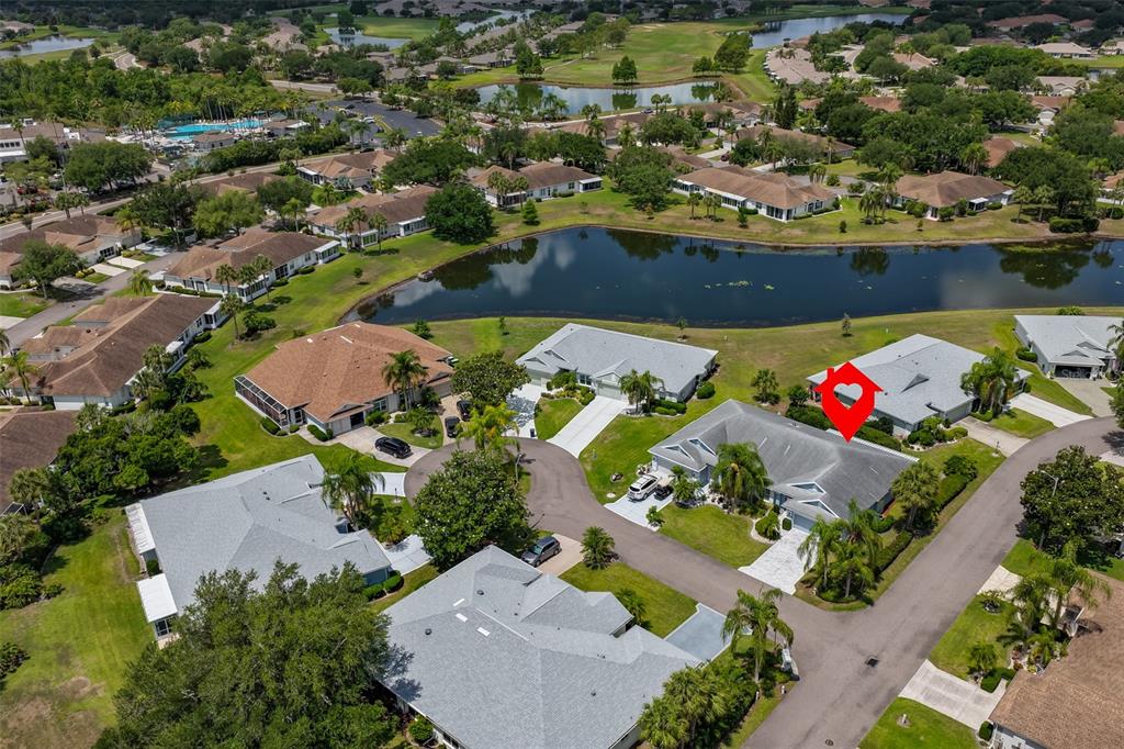 An aerial view shows a residential neighborhood with houses, a pond, and green spaces — 1001 OTTER MILL WAY, SUN CITY CENTER, FL