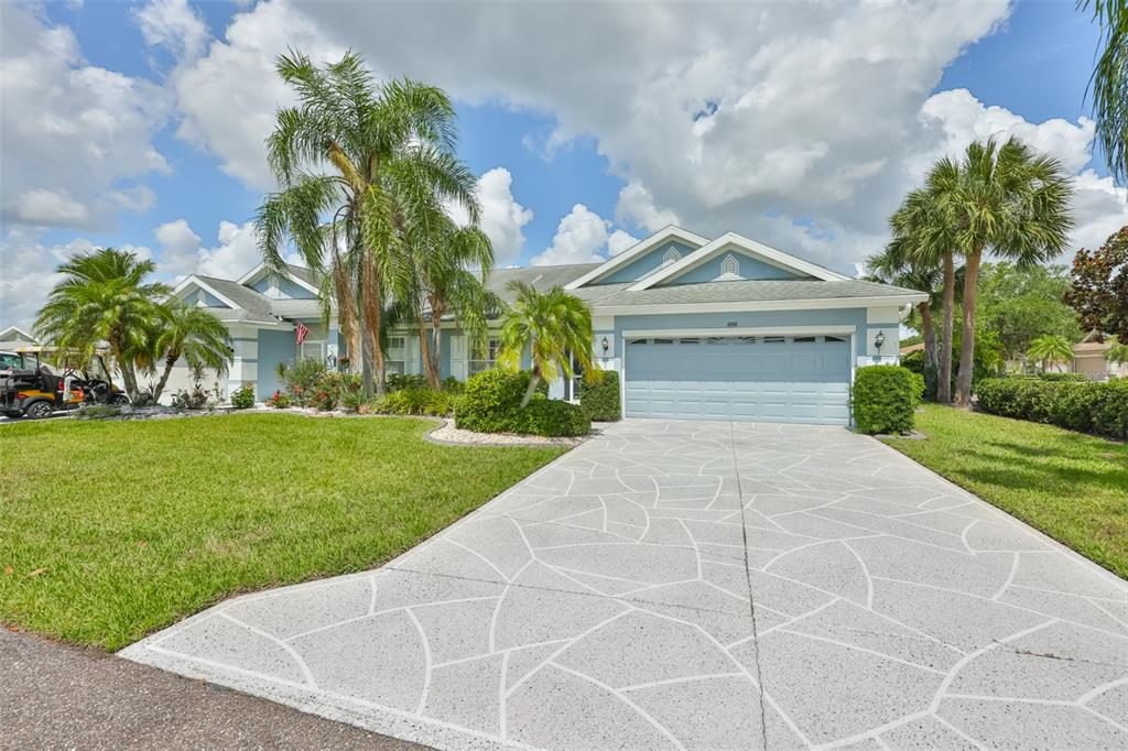 A light blue single-story house features a decorative concrete driveway and several palm trees — 1001 OTTER MILL WAY, SUN CITY CENTER, FL