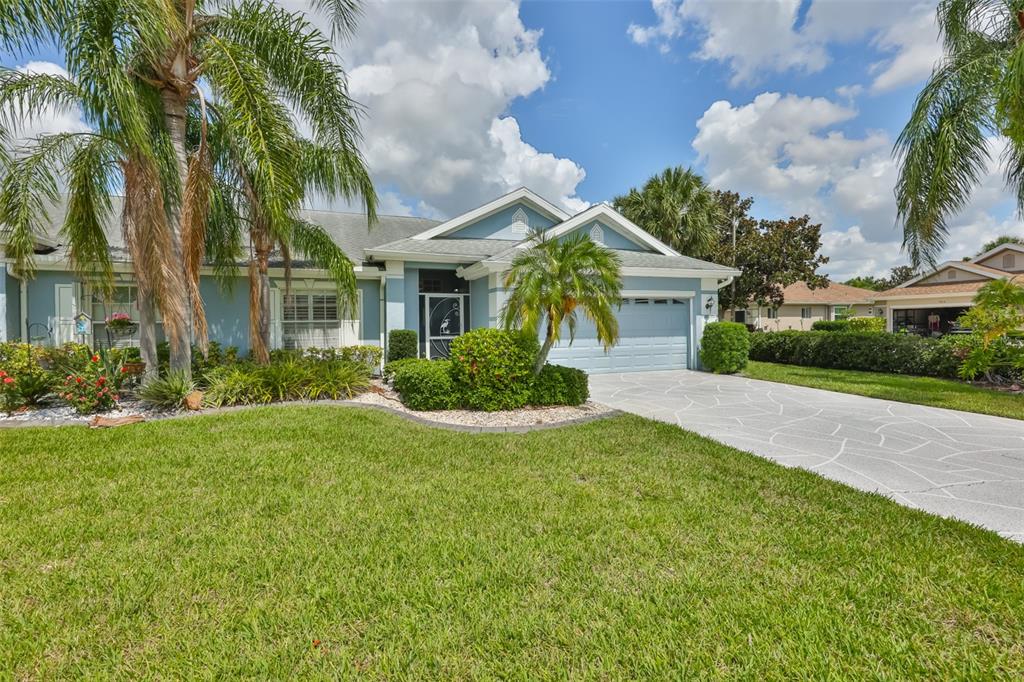 A light blue single-story house features a stone-patterned driveway and palm trees in the yard — 1001 OTTER MILL WAY, SUN CITY CENTER, FL