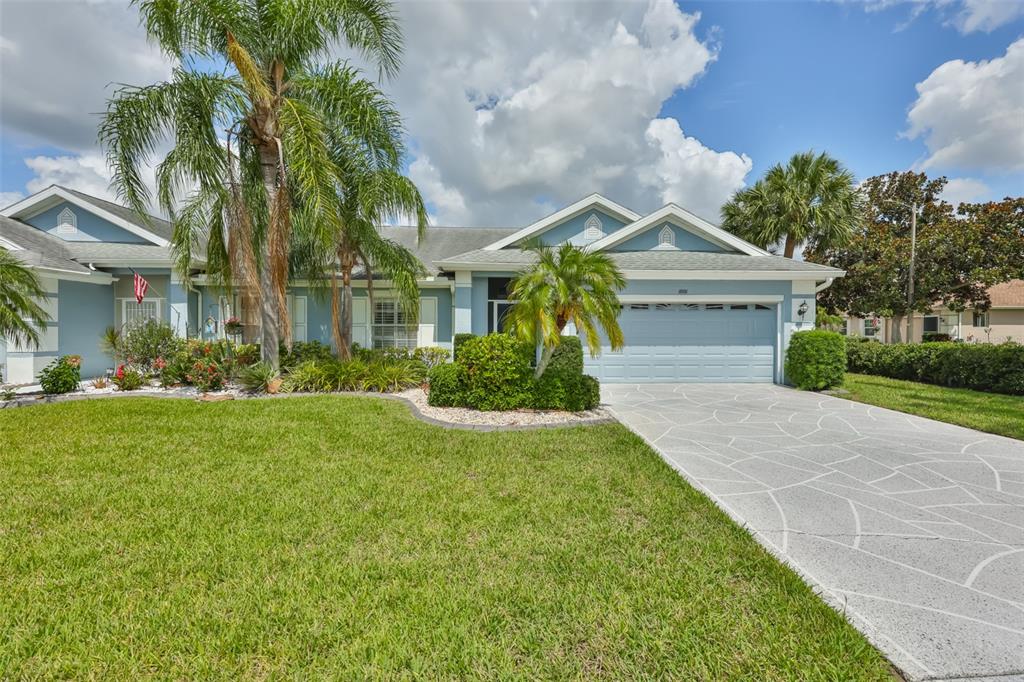 A light blue single-story house features a patterned concrete driveway and a manicured front lawn — 1001 OTTER MILL WAY, SUN CITY CENTER, FL