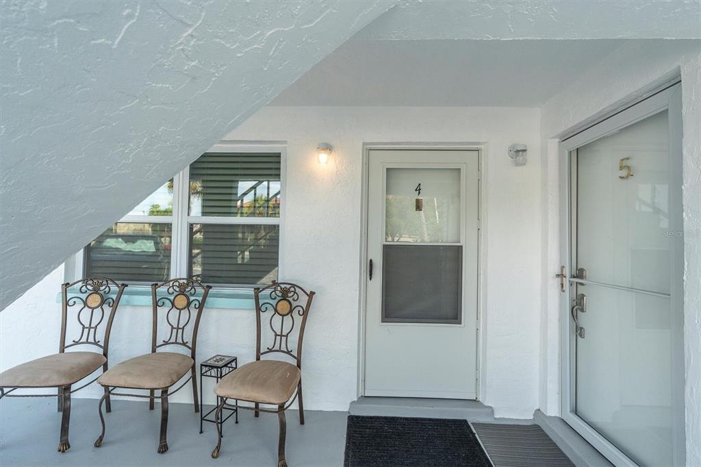 A covered outdoor entryway features three metal chairs, a small table, and two numbered doors — 8800 BLIND PASS ROAD UNIT 4, ST PETE BEACH, FL