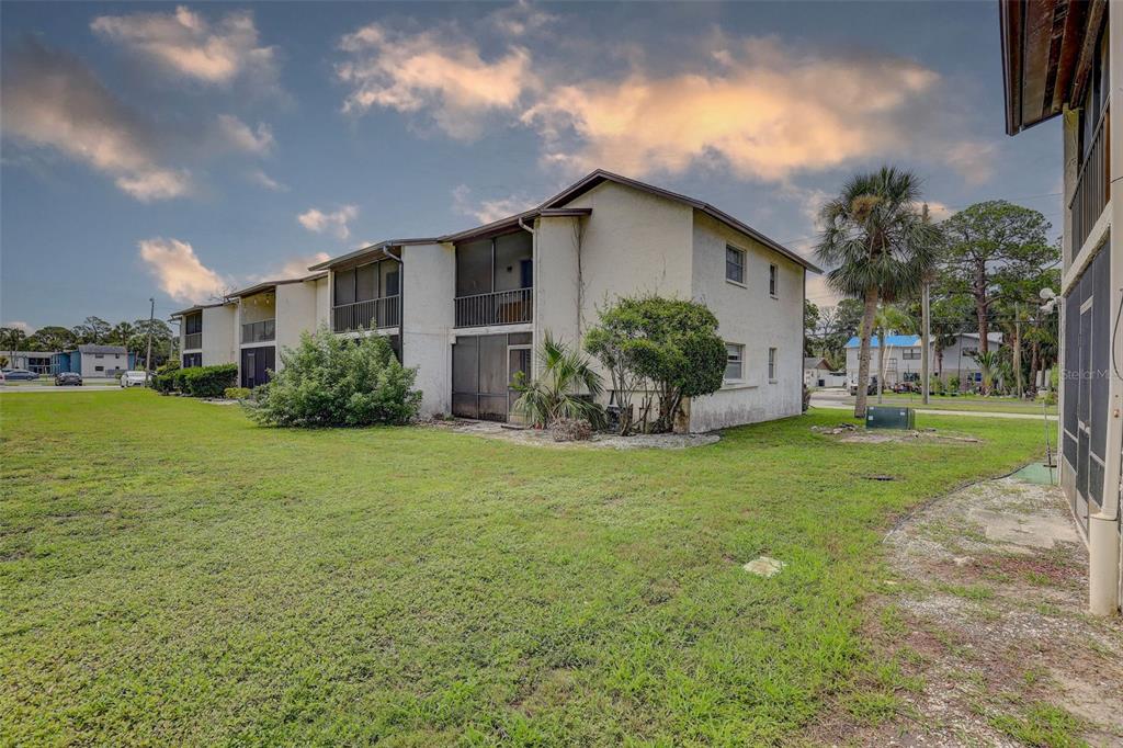 A two-story apartment building with screened balconies sits on a grassy lawn under a cloudy sky — 8440 OLD POST ROAD UNIT 104, PORT RICHEY, FL
