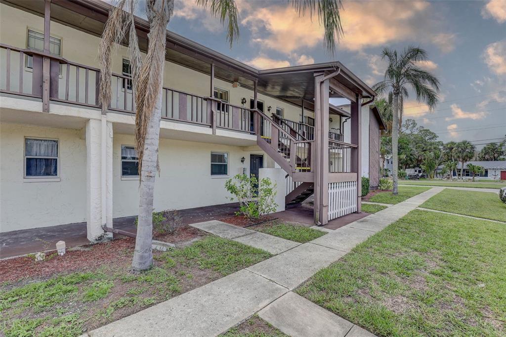 A two-story apartment building exterior features a wooden staircase, balcony, and a concrete walkway — 8440 OLD POST ROAD UNIT 104, PORT RICHEY, FL