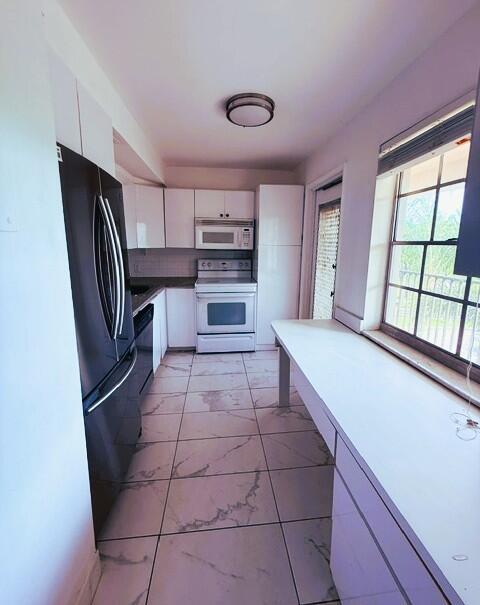 A galley kitchen features white cabinets, stainless steel appliances, and light-colored marble-patterned floor tiles — 3001 S Course Drive # 403, Pompano Beach FL 33069, POMPANO BEACH, FL