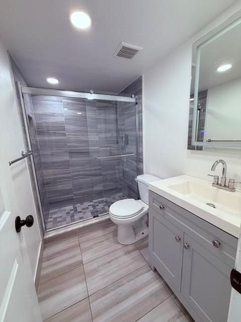 A modern bathroom features a gray vanity, a tiled walk-in shower, and a white toilet — 3001 S Course Drive # 403, Pompano Beach FL 33069, POMPANO BEACH, FL
