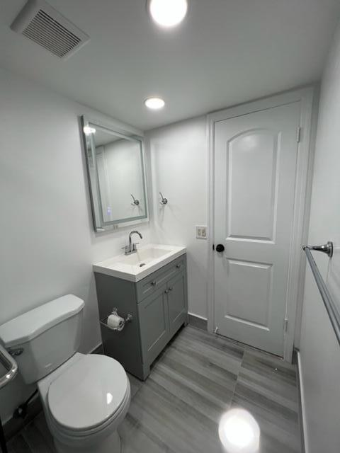 A small bathroom features a gray vanity, a white toilet, and gray wood-look tile flooring — 3001 S Course Drive # 403, Pompano Beach FL 33069, POMPANO BEACH, FL