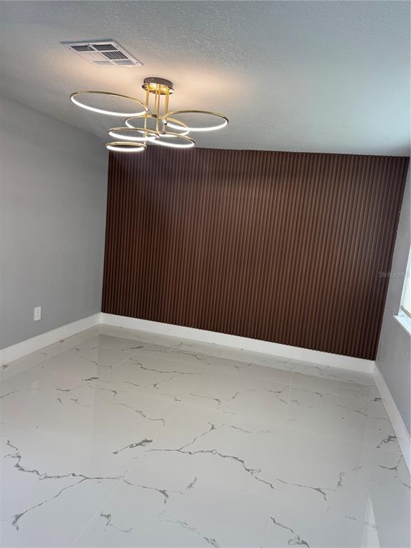 A room with white marble-patterned tile flooring, a dark brown fluted accent wall, and a chandelier — 6205 WESTPORT DRIVE, PORT RICHEY, FL