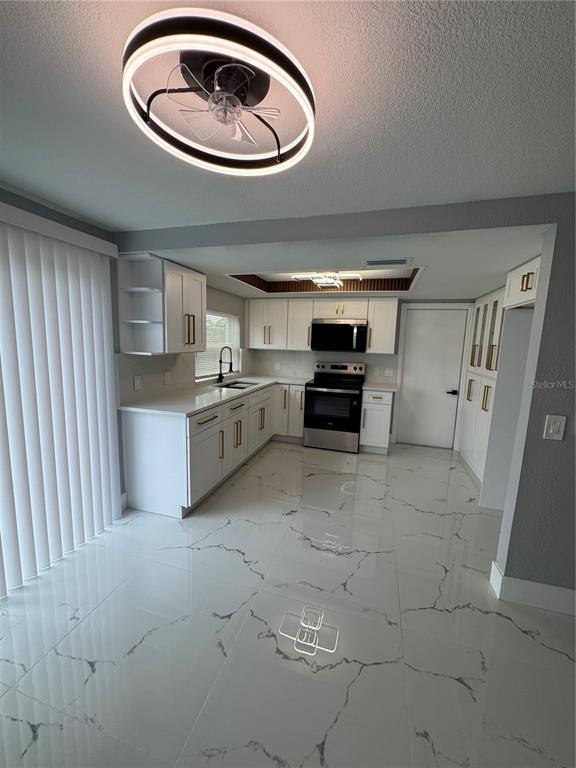 A modern kitchen features white cabinets, gold hardware, stainless steel appliances, and white marble-patterned tile floors — 6205 WESTPORT DRIVE, PORT RICHEY, FL