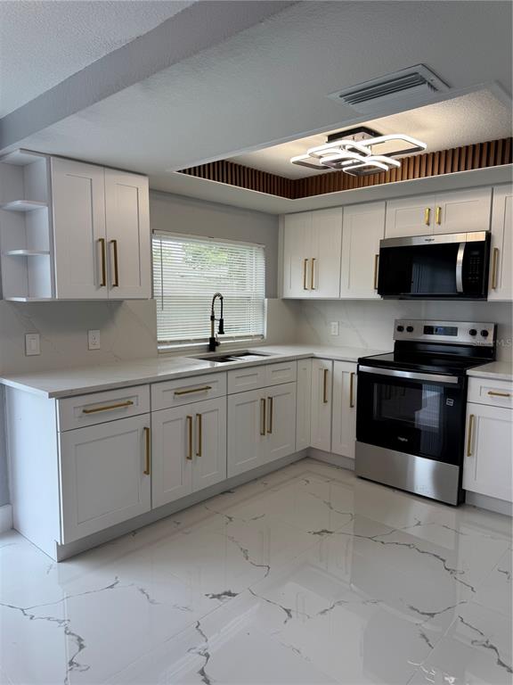 A modern kitchen features white cabinets, gold hardware, stainless steel appliances, and marble-patterned tile floors — 6205 WESTPORT DRIVE, PORT RICHEY, FL