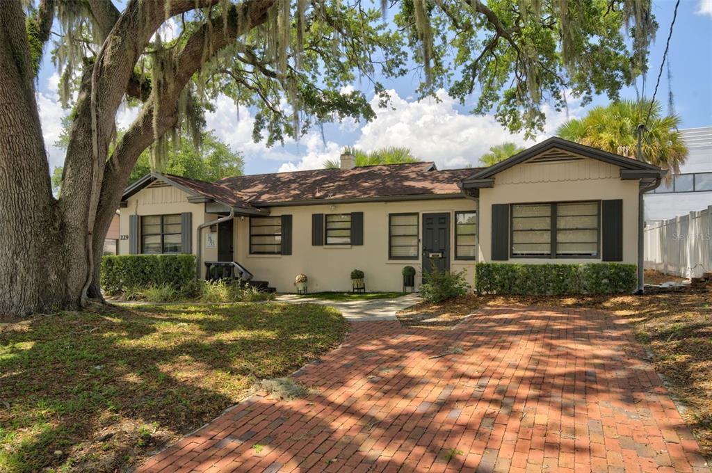 A single-story house with a brick driveway, light-colored stucco walls, and a large oak tree — 229 PASADENA PLACE, ORLANDO, FL