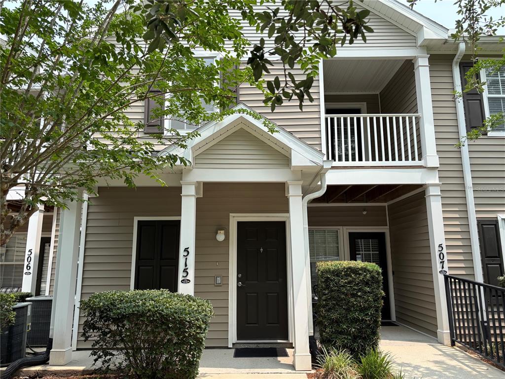 The exterior of a two-story townhouse features beige siding, a covered entryway, and a balcony — 575 OAKLEAF PLANTATION PARKWAY UNIT 515, ORANGE PARK, FL