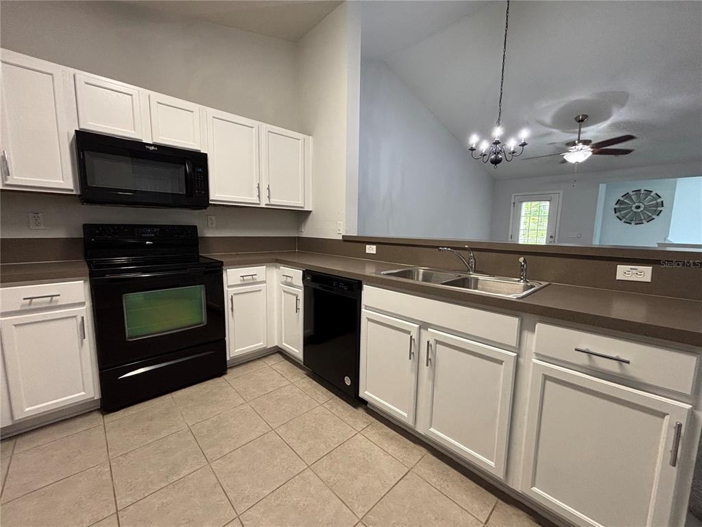 A kitchen features white cabinets, black appliances, a double sink, and tan tile flooring — 575 OAKLEAF PLANTATION PARKWAY UNIT 515, ORANGE PARK, FL