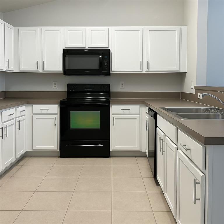 A kitchen features white cabinets, black appliances, and tan countertops over tiled flooring — 575 OAKLEAF PLANTATION PARKWAY UNIT 515, ORANGE PARK, FL