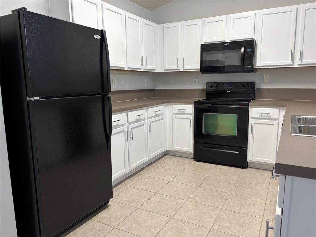 A kitchen features white cabinets, black appliances, brown countertops, and light-colored tile flooring — 575 OAKLEAF PLANTATION PARKWAY UNIT 515, ORANGE PARK, FL