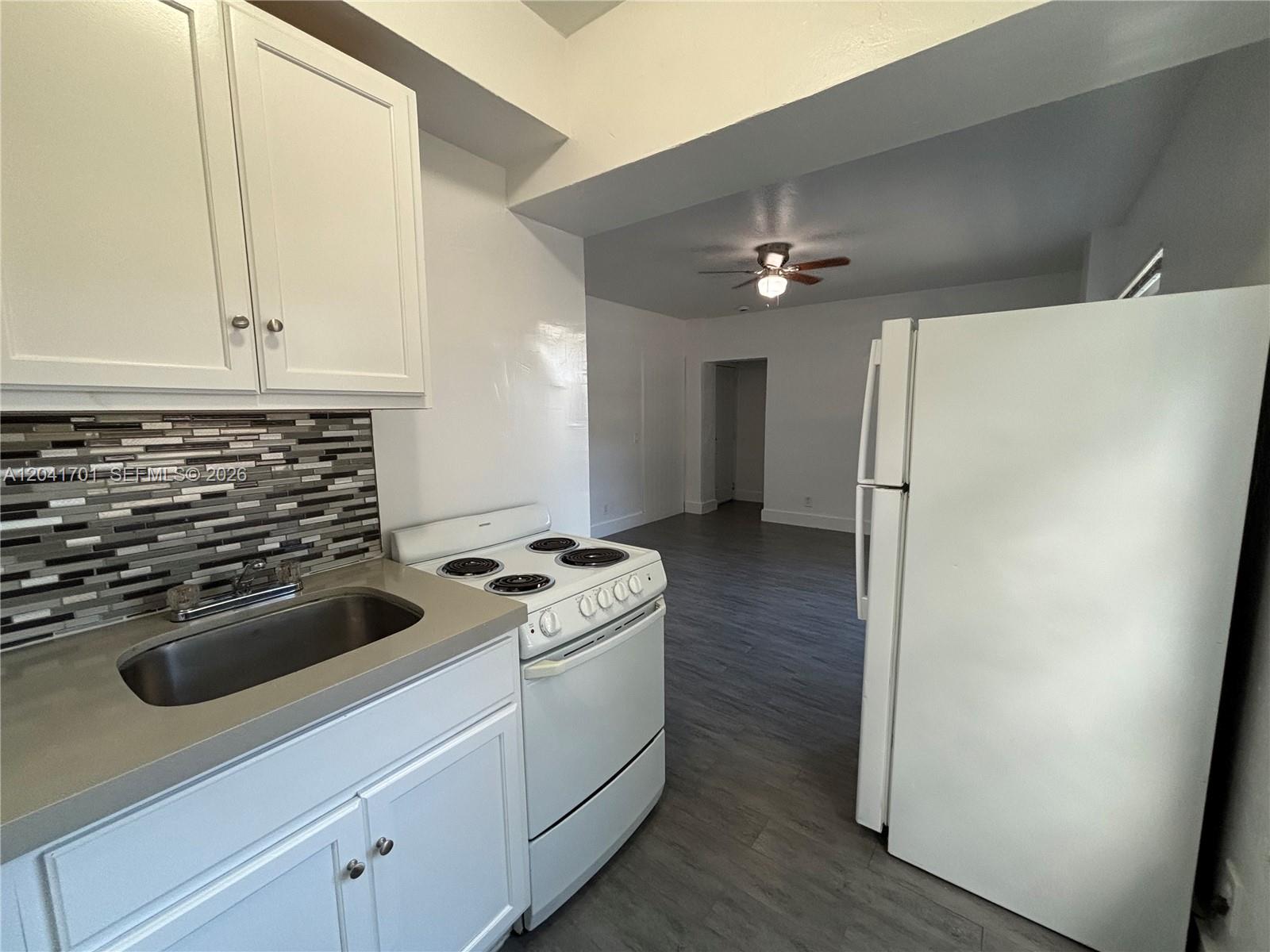 A kitchen features white cabinets, a stainless steel sink, a white stove, and a refrigerator — 1843 Dewey St # 102, Hollywood FL 33020, HOLLYWOOD, FL