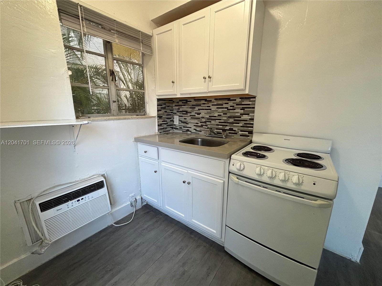 A small kitchen features white cabinets, a tiled backsplash, a sink, and an electric stove — 1843 Dewey St # 102, Hollywood FL 33020, HOLLYWOOD, FL