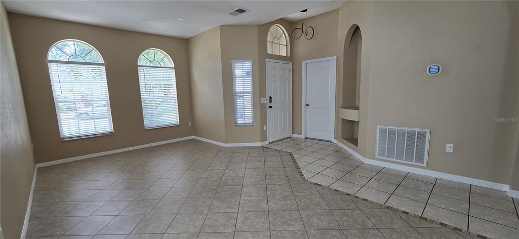 An empty room features beige walls, tile flooring, arched windows, and a white front door — 2227 OAKINGTON STREET, WINTER GARDEN, FL