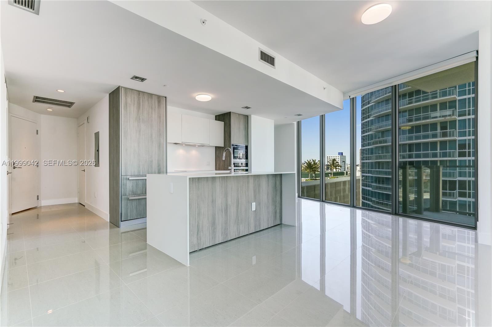 A modern kitchen with wood-grain cabinetry and a white island overlooks a city skyline — 2900 NE 7th Ave # 801, Miami FL 33137, MIAMI, FL