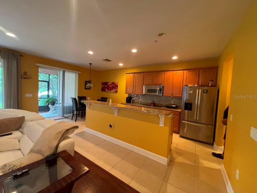 A kitchen with wood cabinets and stainless steel appliances overlooks a living area with tile — 1316 GILFORD POINT LANE, DAVENPORT, FL