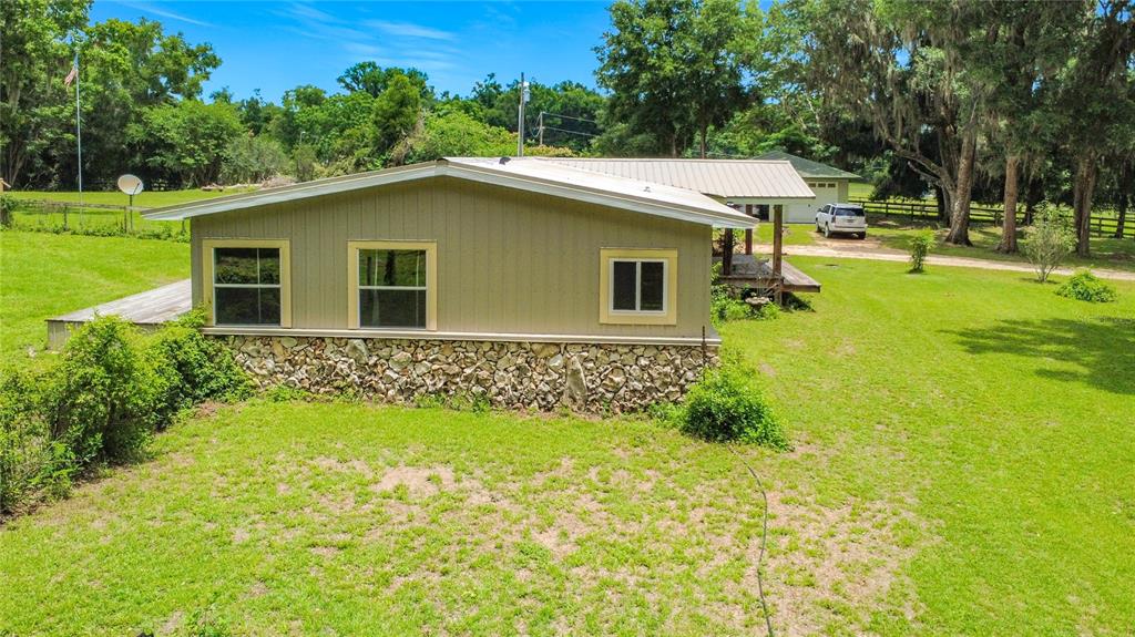 A single-story house with tan siding and a stone foundation sits on a grassy lot — 1919 NW 100TH STREET, OCALA, FL