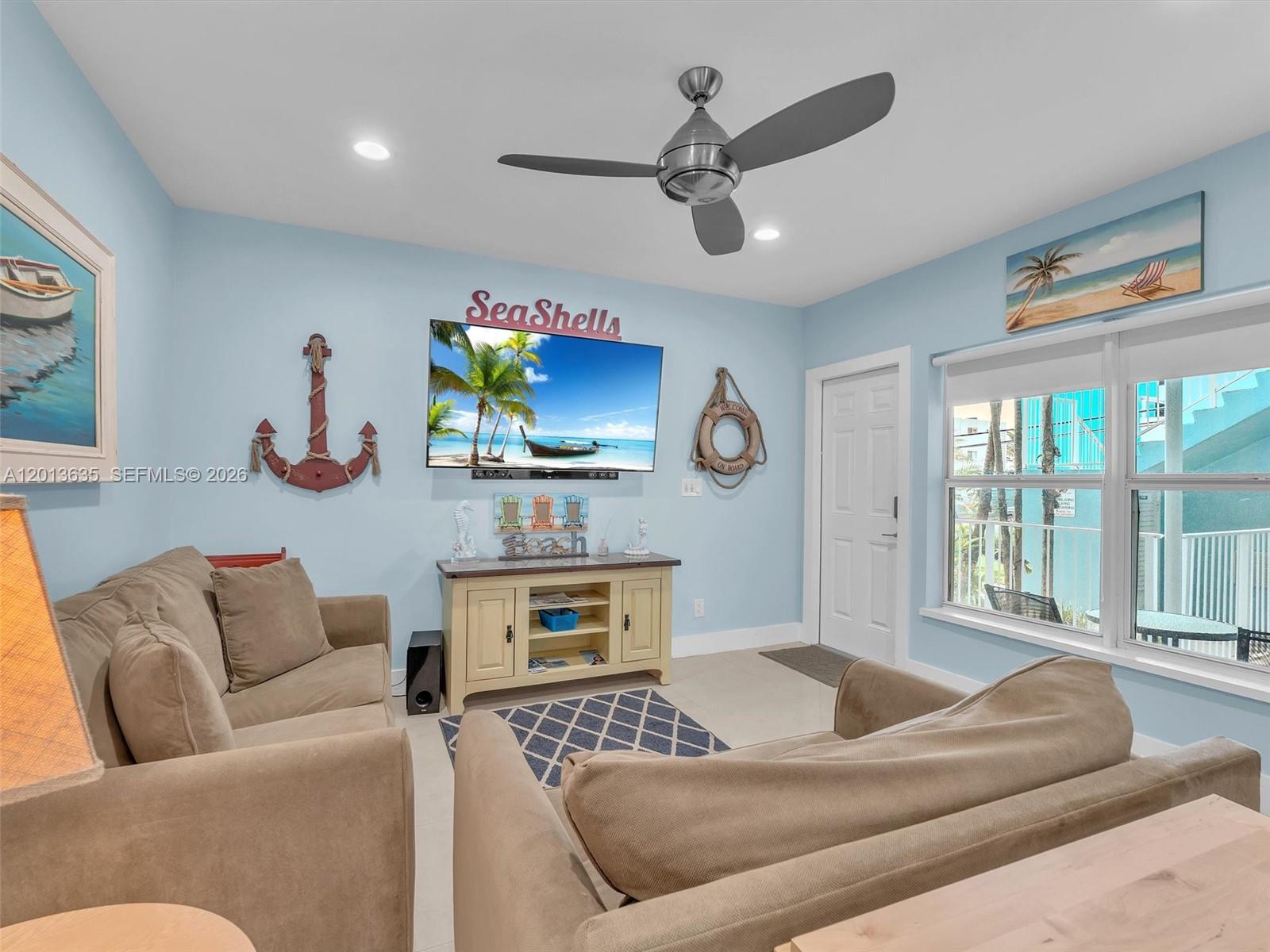 A living room features light blue walls, two beige sofas, a television, and coastal decor — 315 Van Buren St # 103B, Hollywood FL 33019, HOLLYWOOD, FL