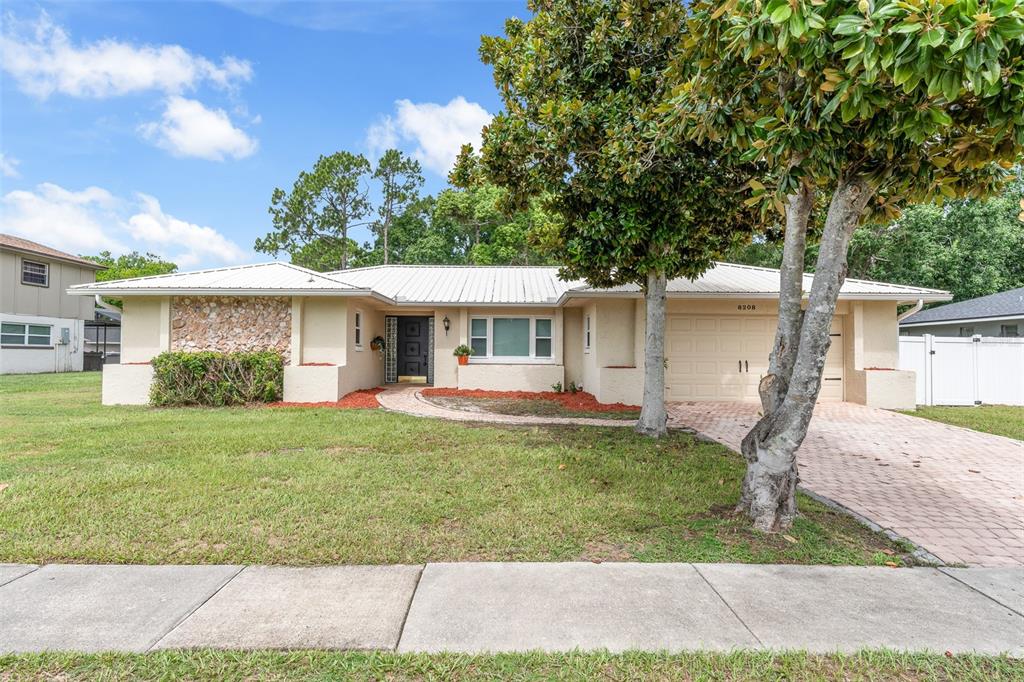 A single-story house with a tan stucco exterior, metal roof, and a paved driveway — 8208 TANSY DRIVE, ORLANDO, FL