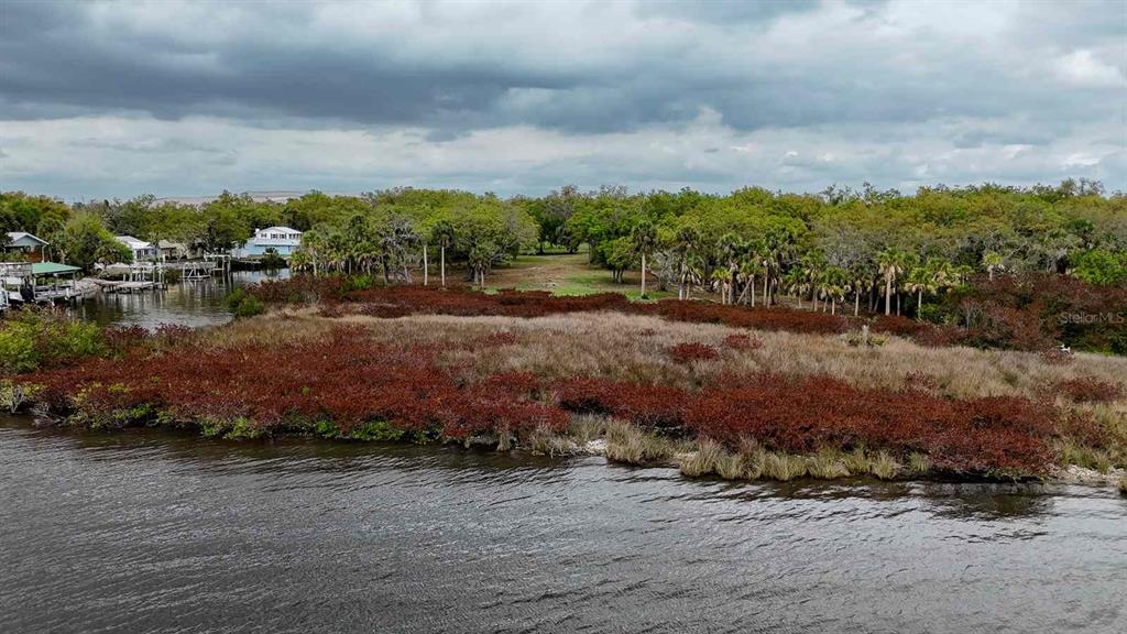 An aerial view shows a waterfront lot with marshy vegetation and trees near a canal — 7013 & 7015 RIVERVIEW DRIVE, RIVERVIEW, FL
