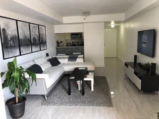 A living room features a white sectional sofa, a gray area rug, and a wall-mounted television — 102 SW 6th Avenue # 206, Miami FL 33130, MIAMI, FL