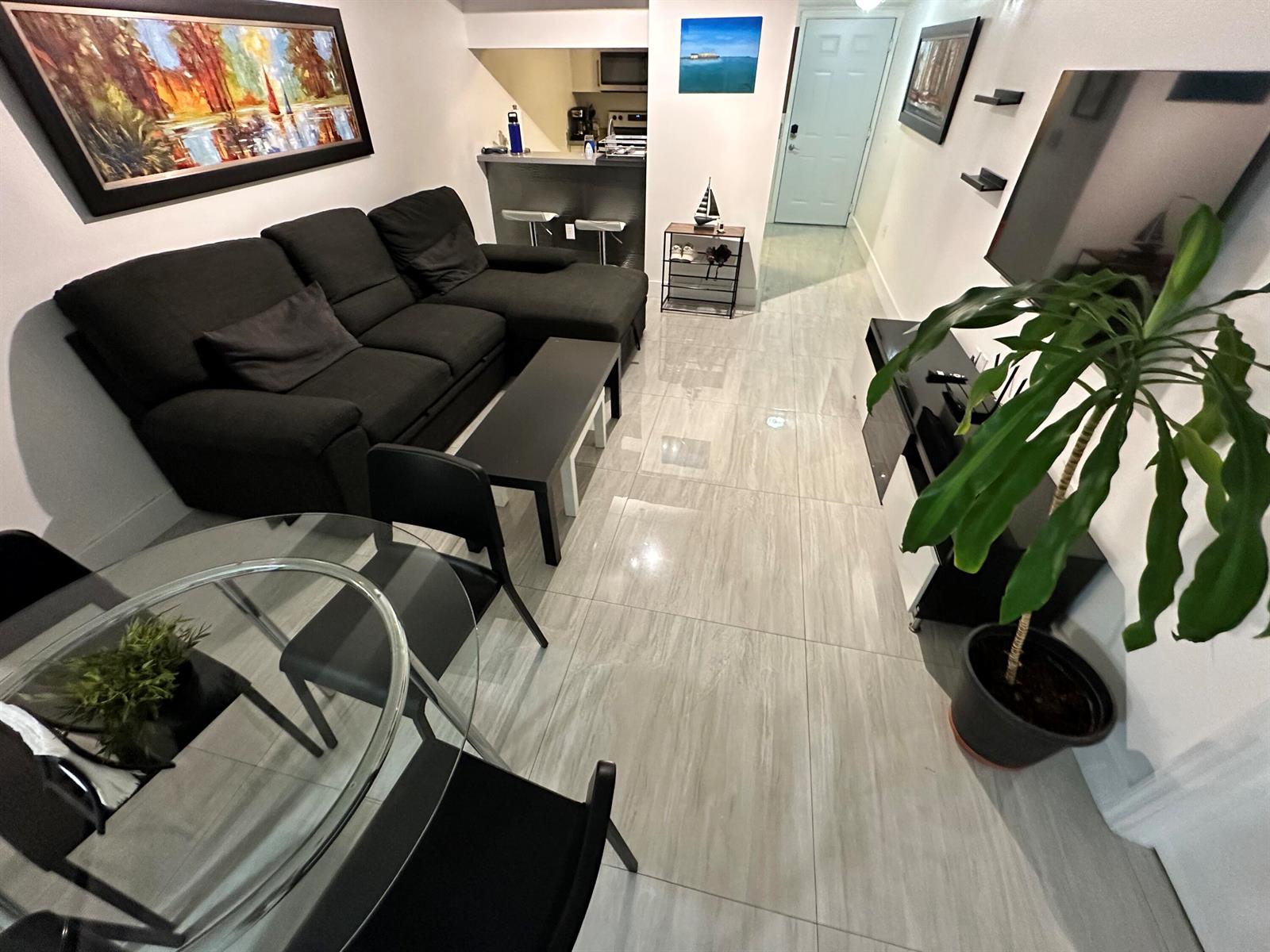 A living room with a black sectional sofa, glass dining table, and light tile flooring — 102 SW 6th Avenue # 206, Miami FL 33130, MIAMI, FL