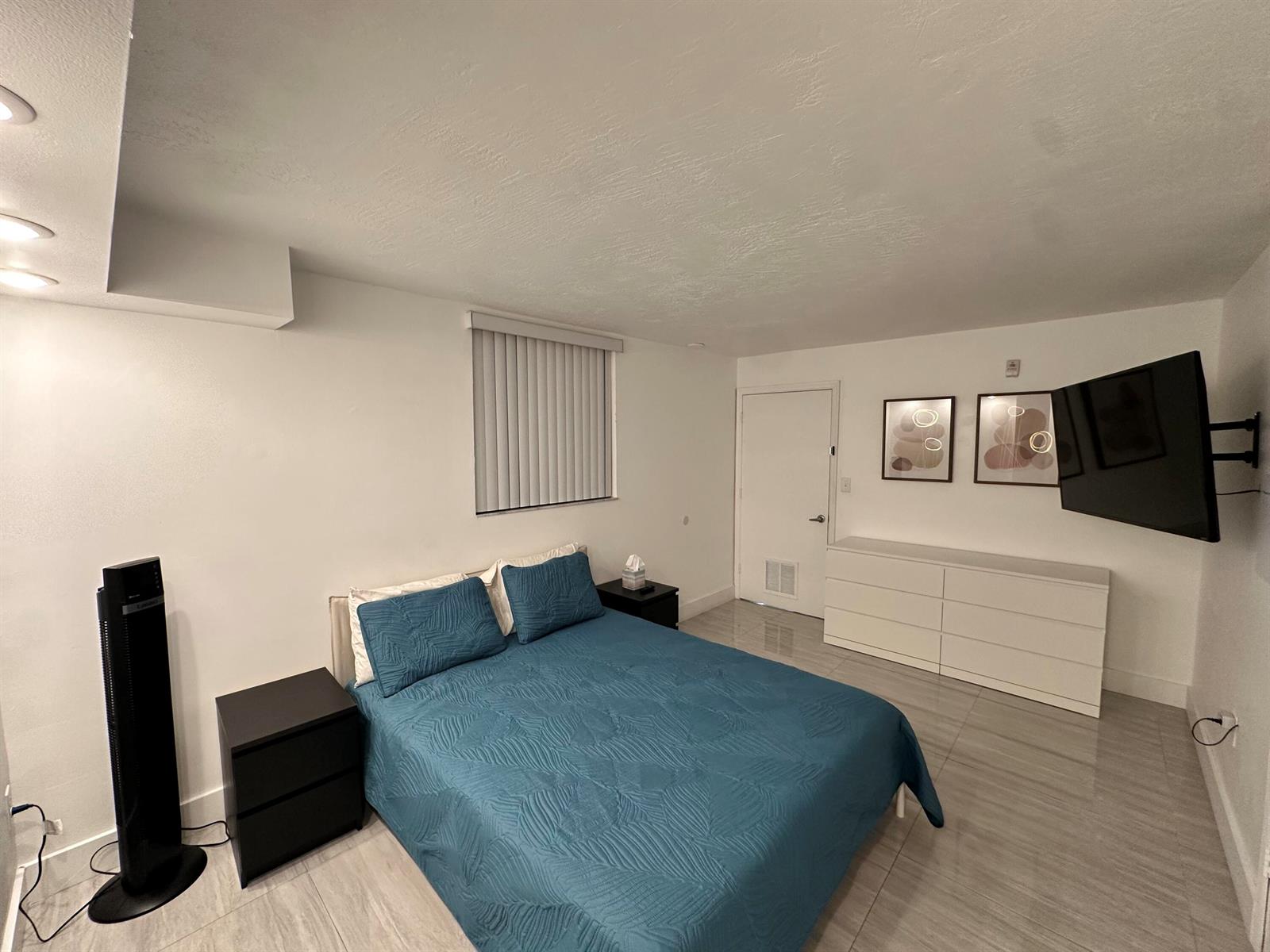 A bedroom features a teal bedspread, white dresser, wall-mounted television, and light-colored tile flooring — 102 SW 6th Avenue # 206, Miami FL 33130, MIAMI, FL