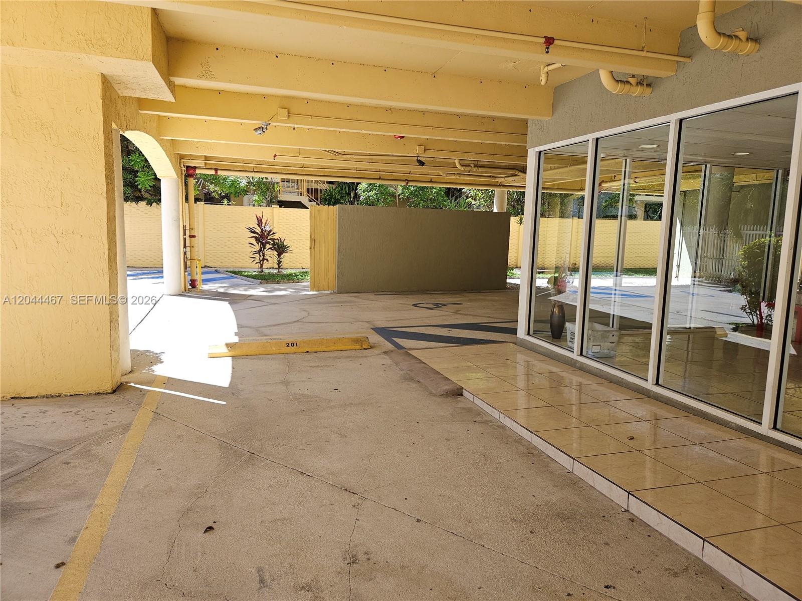 A covered parking area features a concrete floor, yellow support beams, and glass-walled building access — 437 SW 7th St # 201, Miami FL 33130, MIAMI, FL