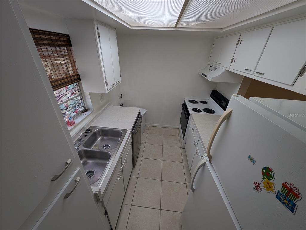 A galley kitchen features white cabinets, white appliances, a double sink, and light-colored tile flooring — 2524 SE 15TH AVENUE UNIT B, OCALA, FL