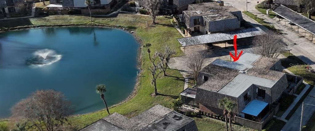An aerial view shows a multi-unit residential building with a flat roof next to a pond — 1004 ROYAL OAK BOULEVARD, LEESBURG, FL