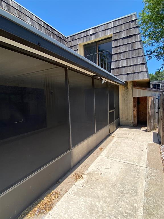 A screened-in patio sits beside a concrete walkway and a house with wood-shingled siding — 1004 ROYAL OAK BOULEVARD, LEESBURG, FL