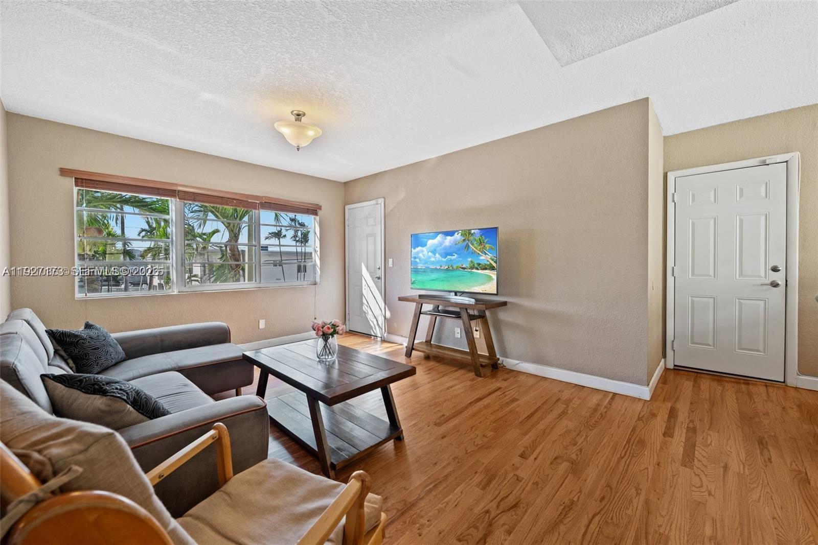 A living room features hardwood floors, a grey sofa, a coffee table, and a television — 8345 Byron Ave # 6, Miami Beach FL 33141, MIAMI BEACH, FL