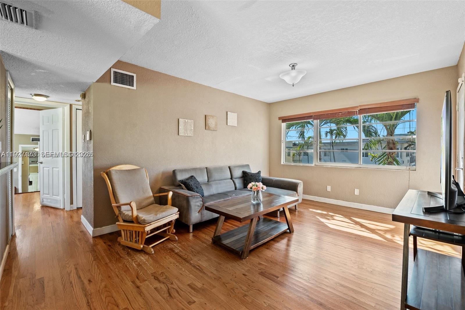 A living room features hardwood floors, a gray sofa, a rocking chair, and a window — 8345 Byron Ave # 6, Miami Beach FL 33141, MIAMI BEACH, FL