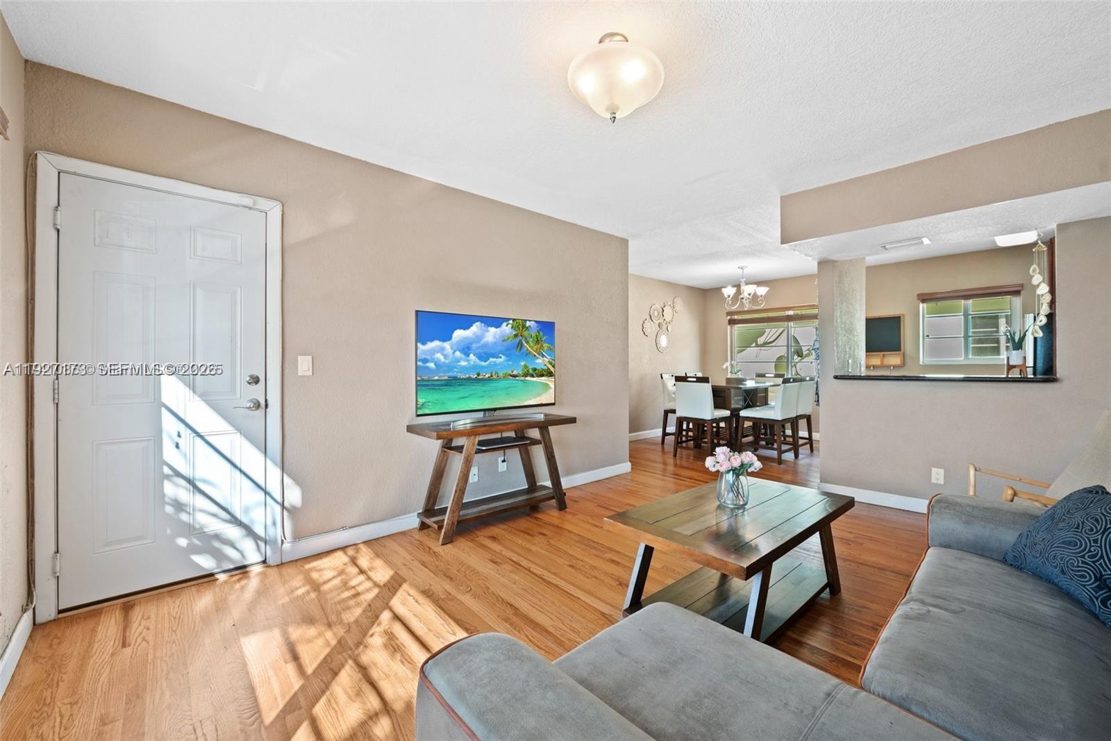 A living room with hardwood floors, a television on a stand, and an adjacent dining area — 8345 Byron Ave # 6, Miami Beach FL 33141, MIAMI BEACH, FL