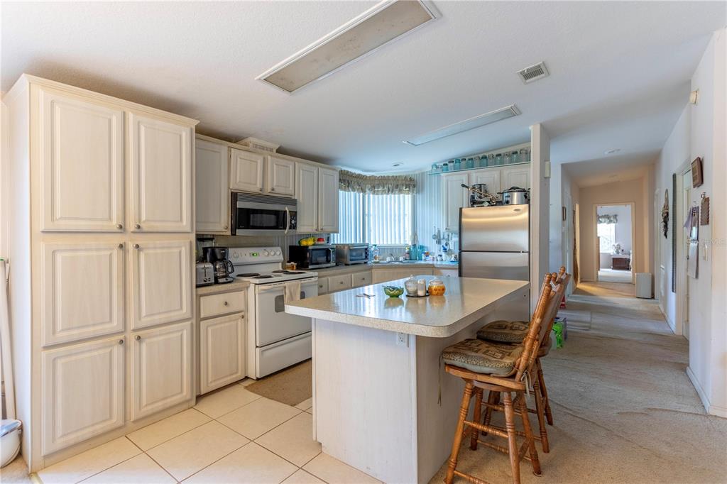 A kitchen features white cabinetry, a central island with bar stools, and tile flooring — 2600 WACCASSA STREET, GENEVA, FL
