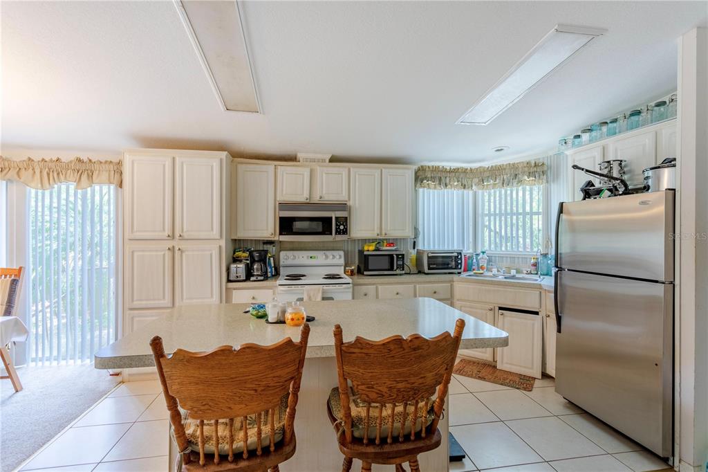A kitchen features white cabinetry, a central island with two wooden chairs, and stainless appliances — 2600 WACCASSA STREET, GENEVA, FL