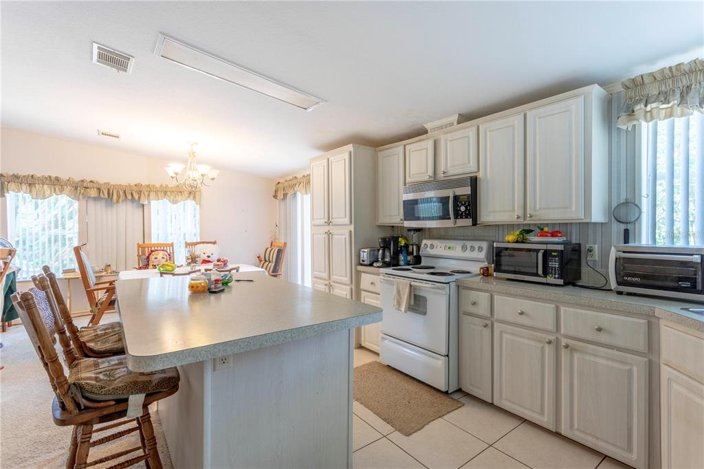 A kitchen features white cabinetry, a central island with seating, and an adjacent dining area — 2600 WACCASSA STREET, GENEVA, FL
