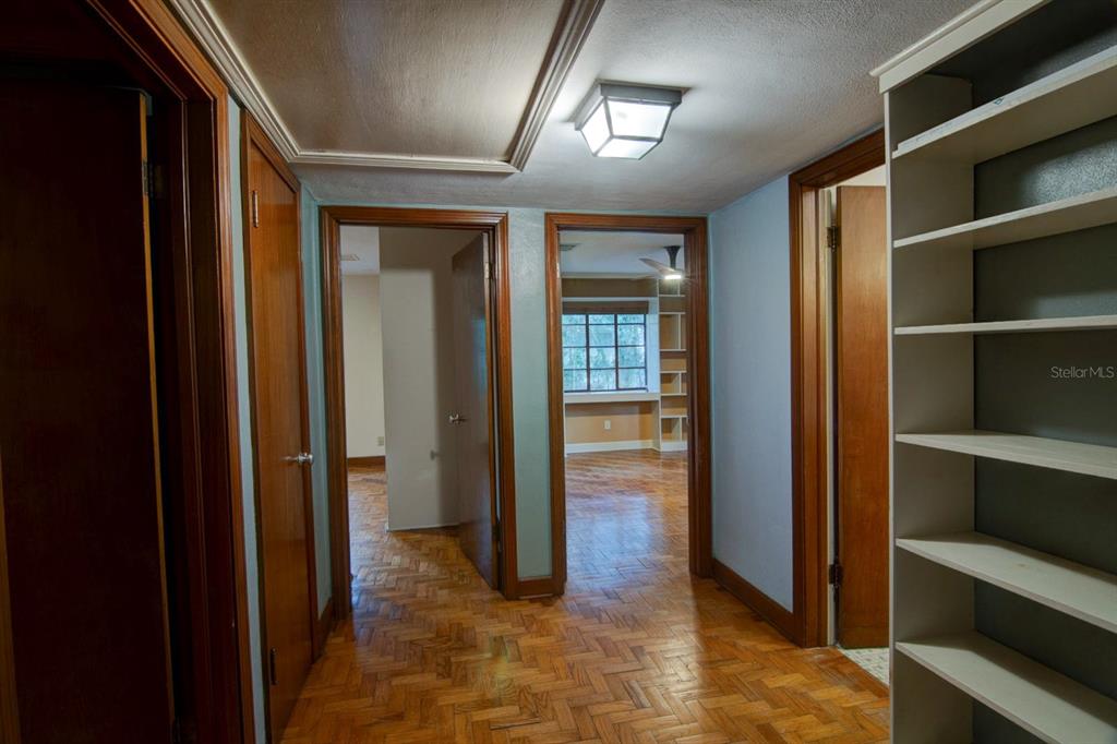 A hallway with parquet flooring leads to two doorways and features built-in shelving — 2049 NW 9TH AVENUE, GAINESVILLE, FL