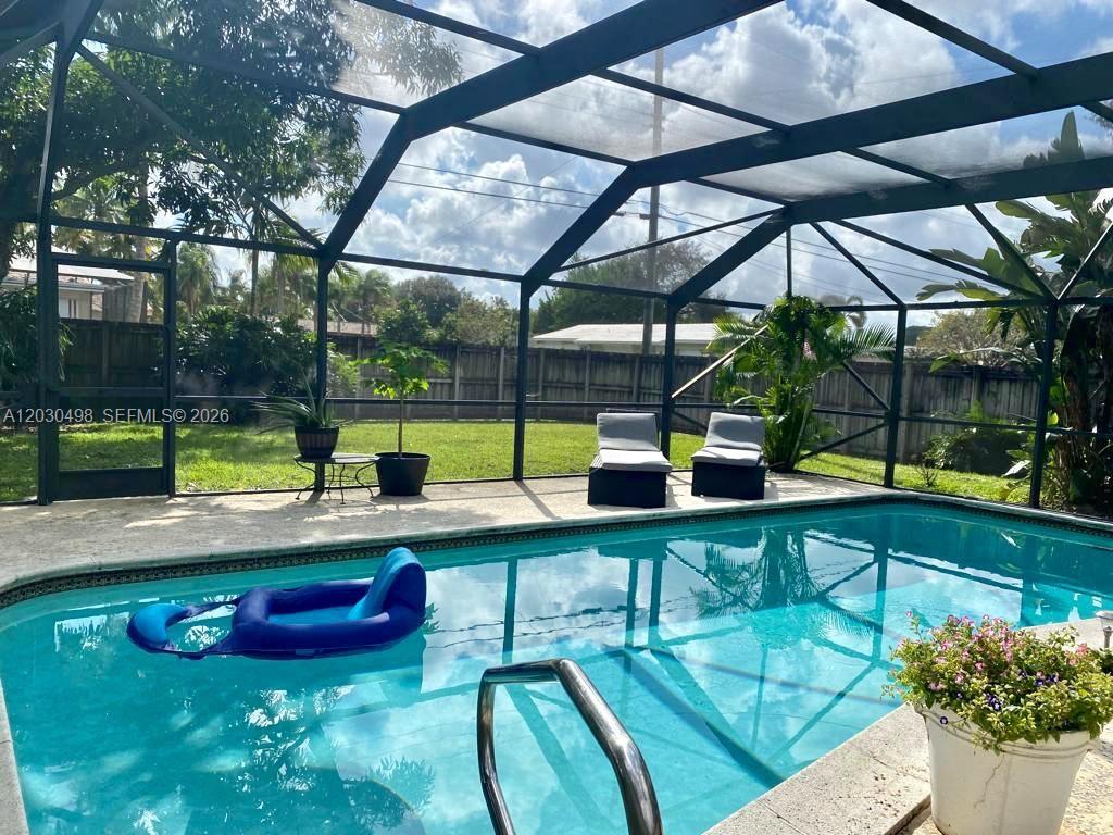 A swimming pool with a blue float sits inside a screened-in patio enclosure — 4116 Taft St, Hollywood FL 33021, HOLLYWOOD, FL