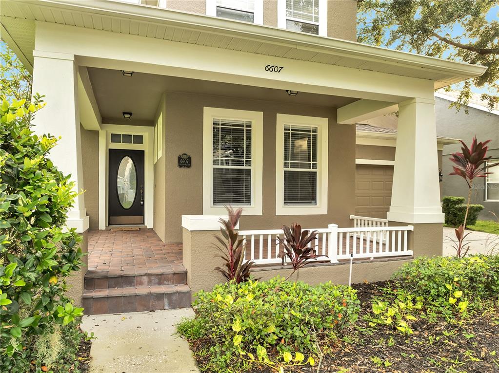 A tan house exterior features a covered front porch with white railings and columns — 6607 EARTHGOLD DRIVE, WINDERMERE, FL