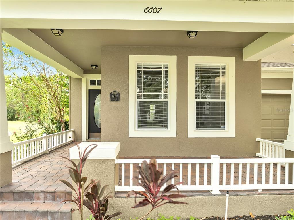 The exterior of a house features a covered front porch with white railings and pavers — 6607 EARTHGOLD DRIVE, WINDERMERE, FL