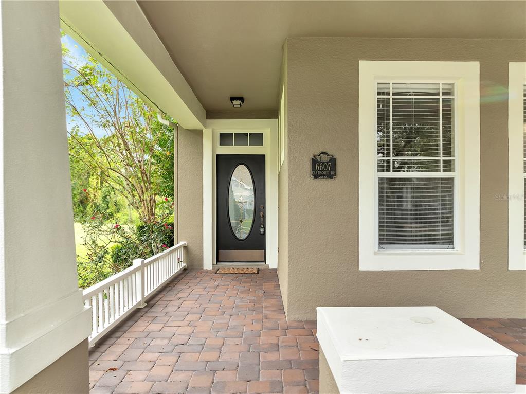 A covered front porch features a brick paver floor, white railing, and a dark front door — 6607 EARTHGOLD DRIVE, WINDERMERE, FL