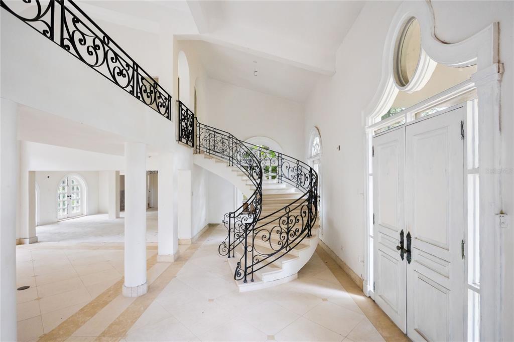 A bright foyer features a curved staircase with ornate black iron railings and white tile floors — Urb. San Patricio RIVERA FERRER ST. UNIT 30, GUAYNABO, PR